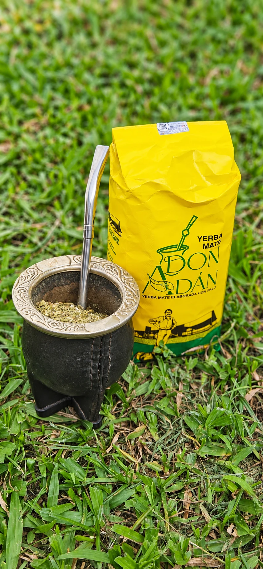Mate con bombilla junto a un paquete de yerba mate Don Adán sobre el pasto